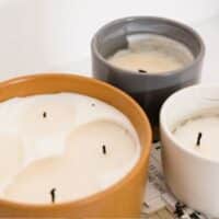Three candles with varying sizes and wax levels, infused with fragrance oil for candles, set on a light surface. The leftmost is large and terracotta-colored, the middle is medium in gray,