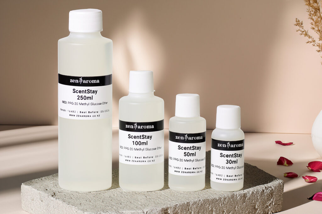 Image showing four bottles of various sizes, all labeled "ScentStay" by zenAroma. The bottles, ranging from 30ml to 250ml, stand on a textured slab against a neutral background. Rose petals are scattered to the side, adding a touch of color to the minimalist setting, emphasizing ScentStay's role as a fragrance fixative.